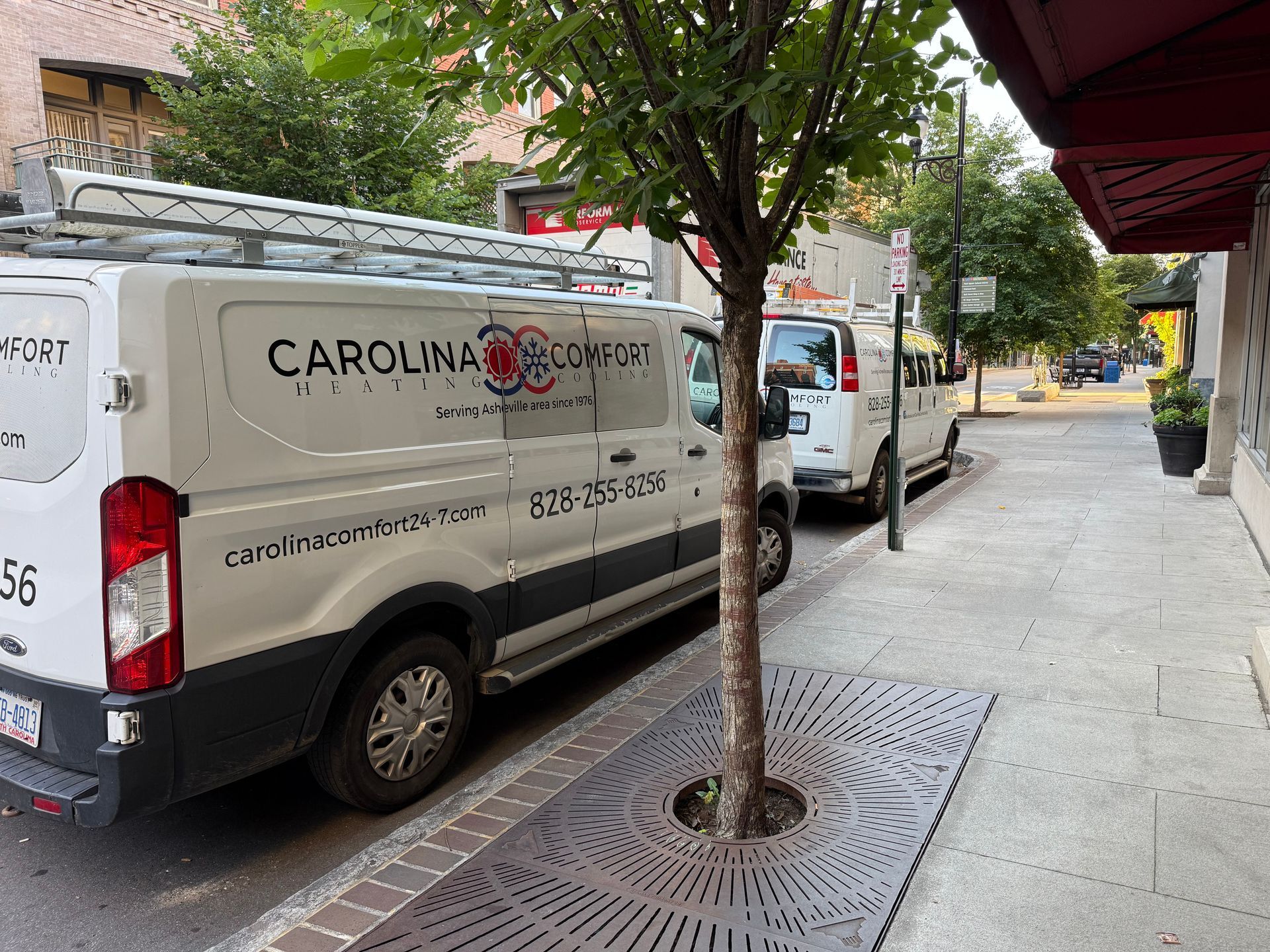 White Carolina Comfort van parked on a city street, tree in the foreground.