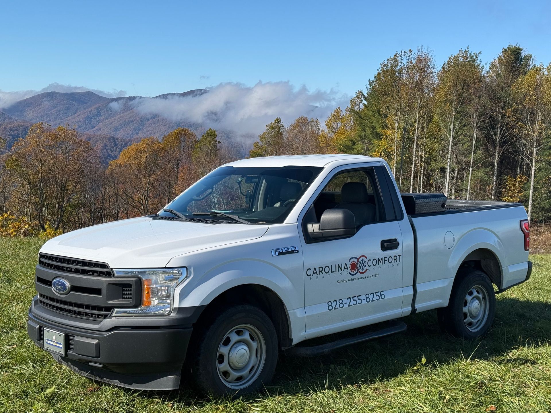 White Ford pickup truck with logo parked on a grassy hill overlooking a mountain range.