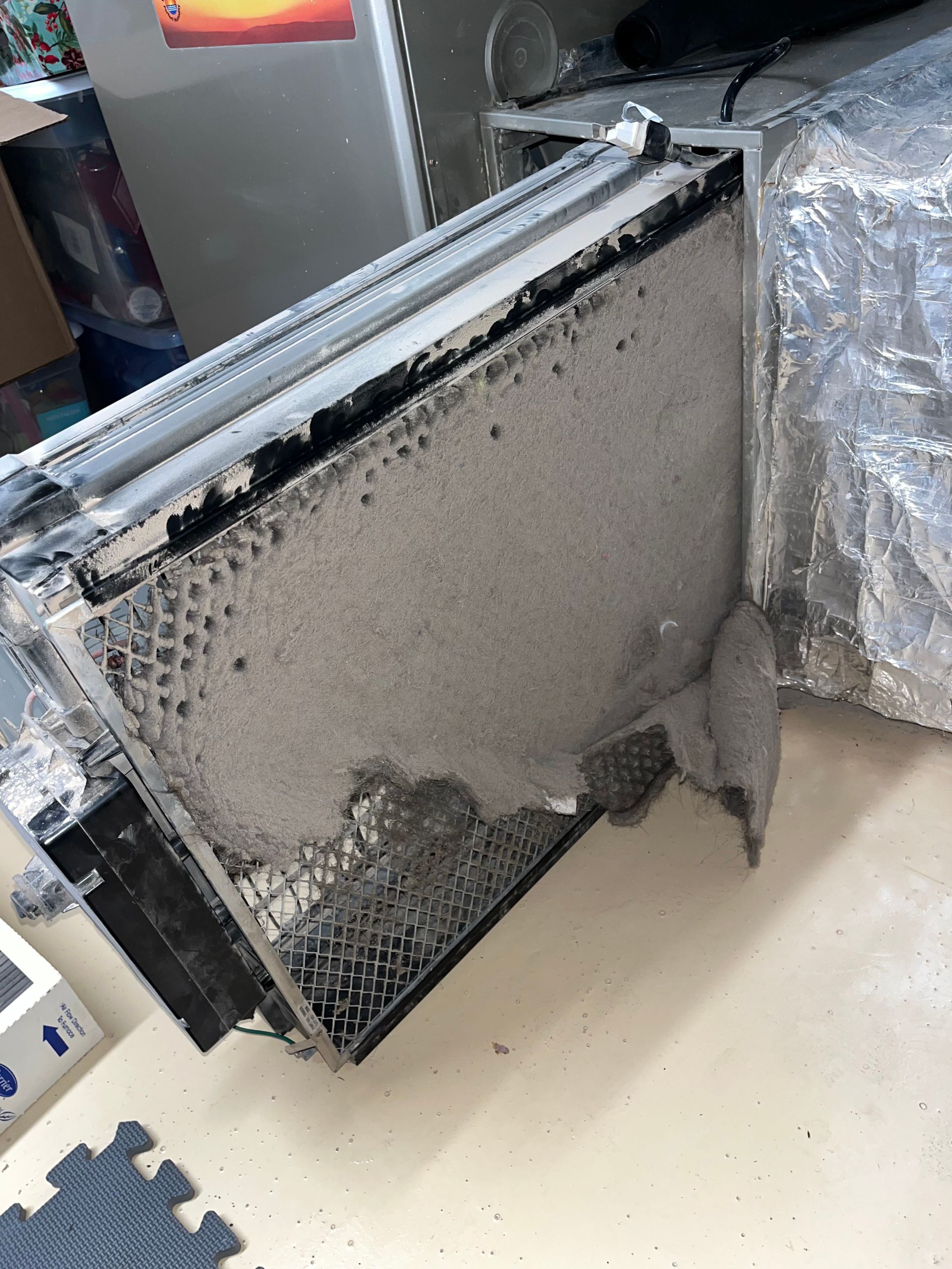 Dirty HVAC filter caked with gray dust and debris, inside an air duct.