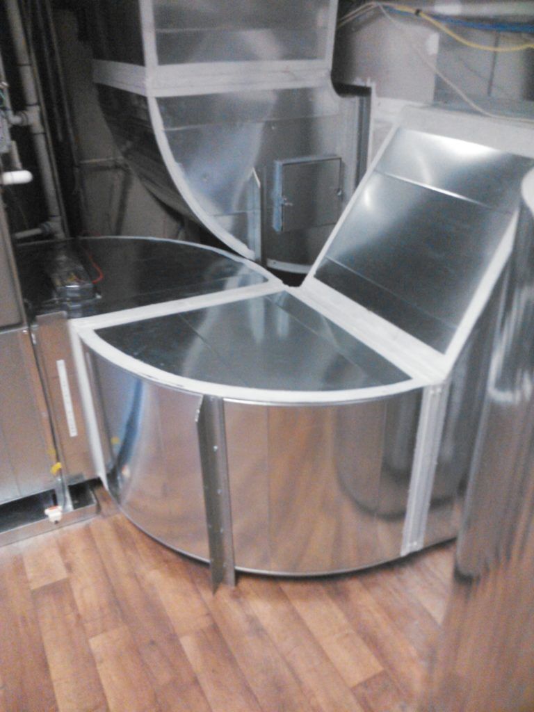 A metal duct is sitting on a wooden floor in a room.