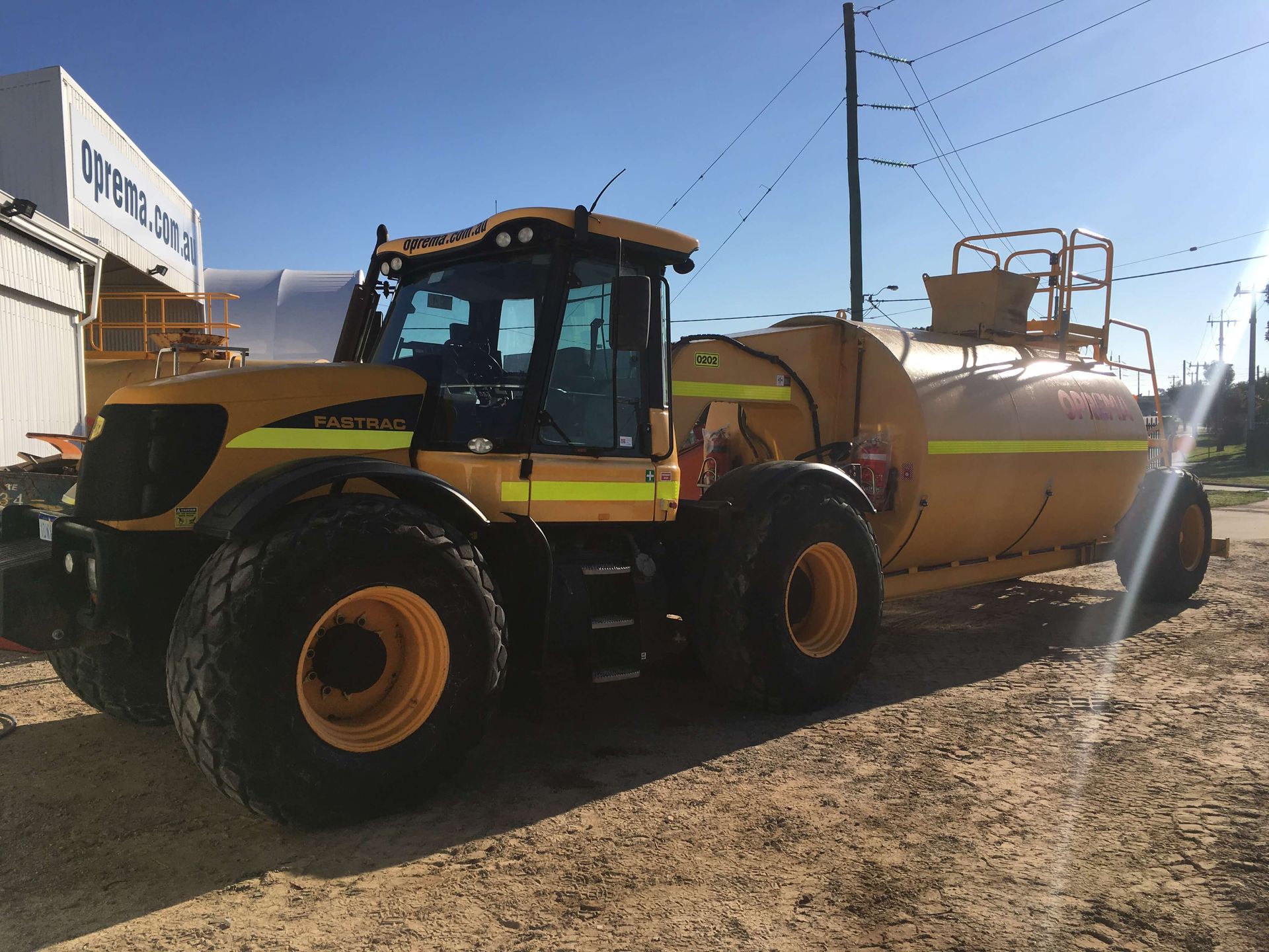 A yellow tractor with a tank attached to it is parked in a dirt lot.