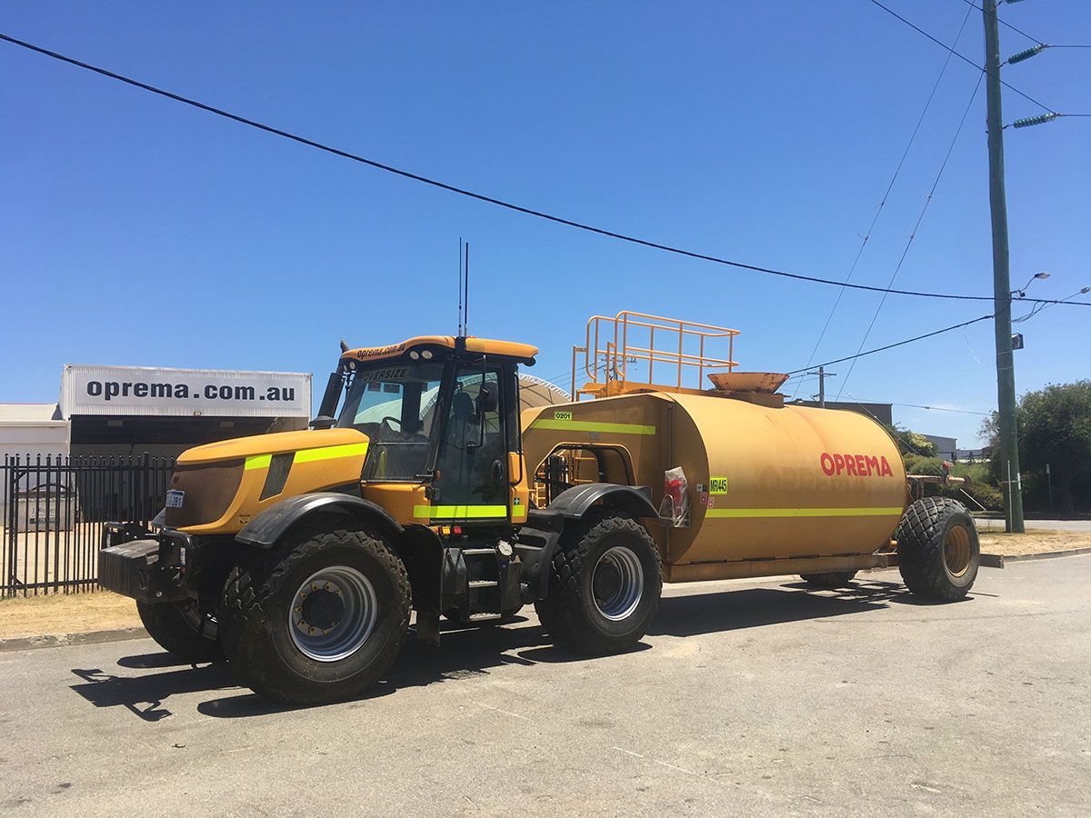 A yellow tractor with a large tank attached to it is parked on the side of the road.
