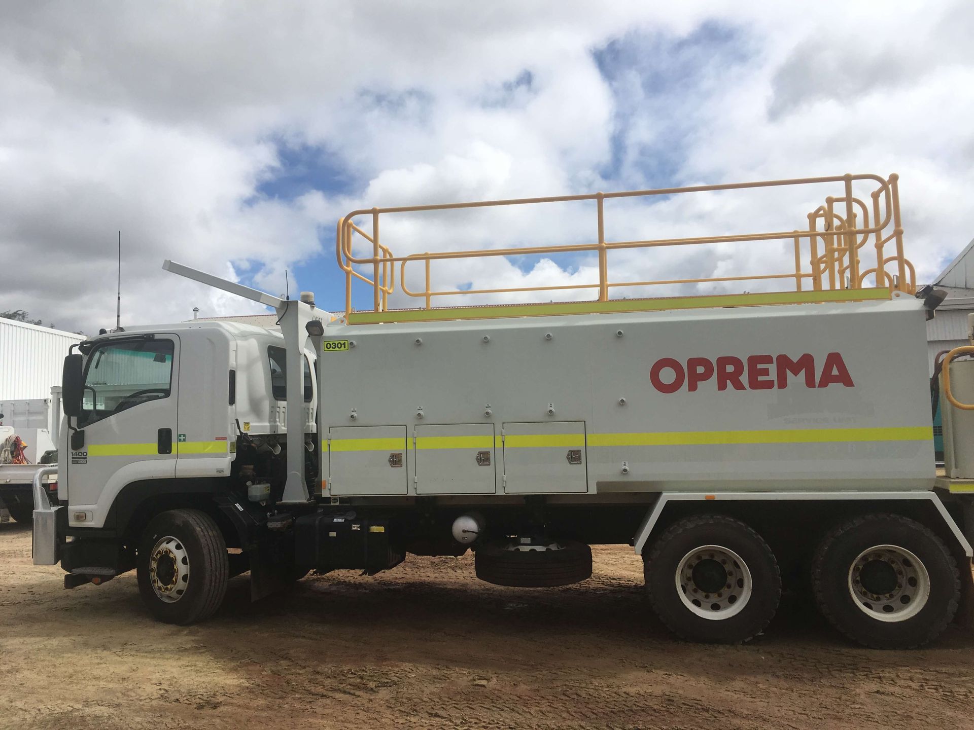 A white truck with the word oprema on the side is parked in a dirt lot.