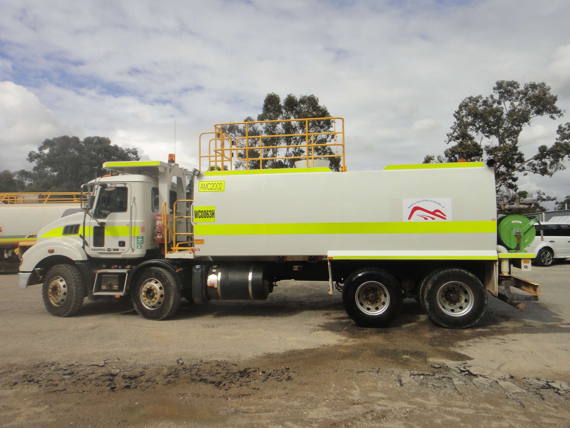 A white truck with yellow stripes on the side is parked in a parking lot.