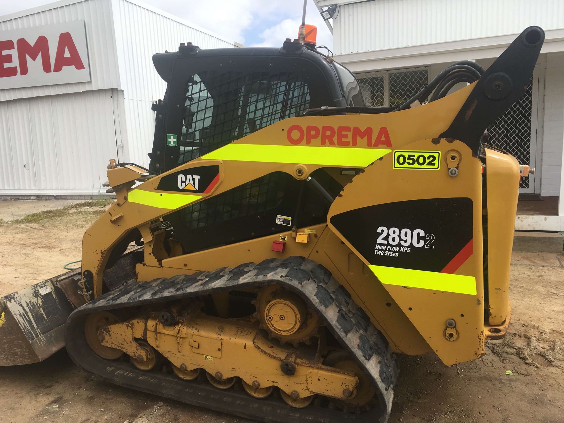 A cat bulldozer is parked in front of a building that says oprema