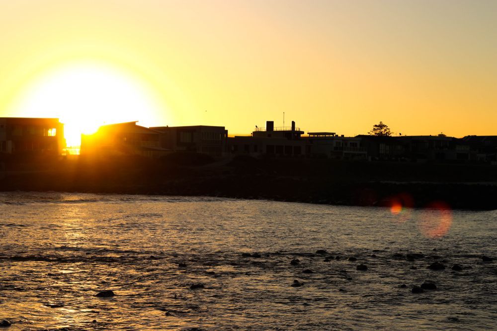 Sunset Over Water With Silhouetted Buildings and Reflections — Fair Plumbing In Shellharbour, NSW