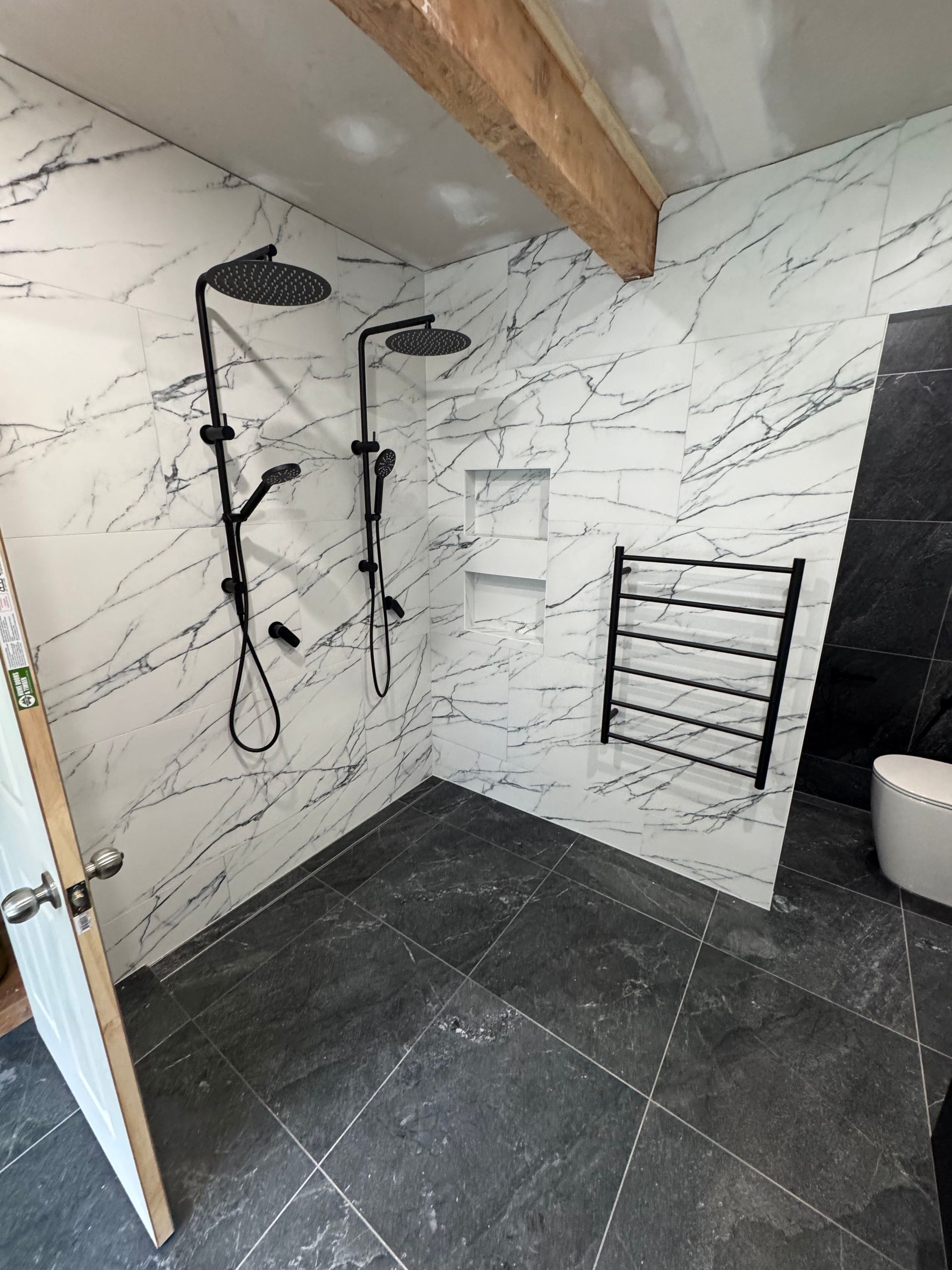 Bathroom with black fixtures, marble-patterned walls, dark tile floor, black towel rack, and a toilet — Fair Plumbing In Shellharbour, NSW