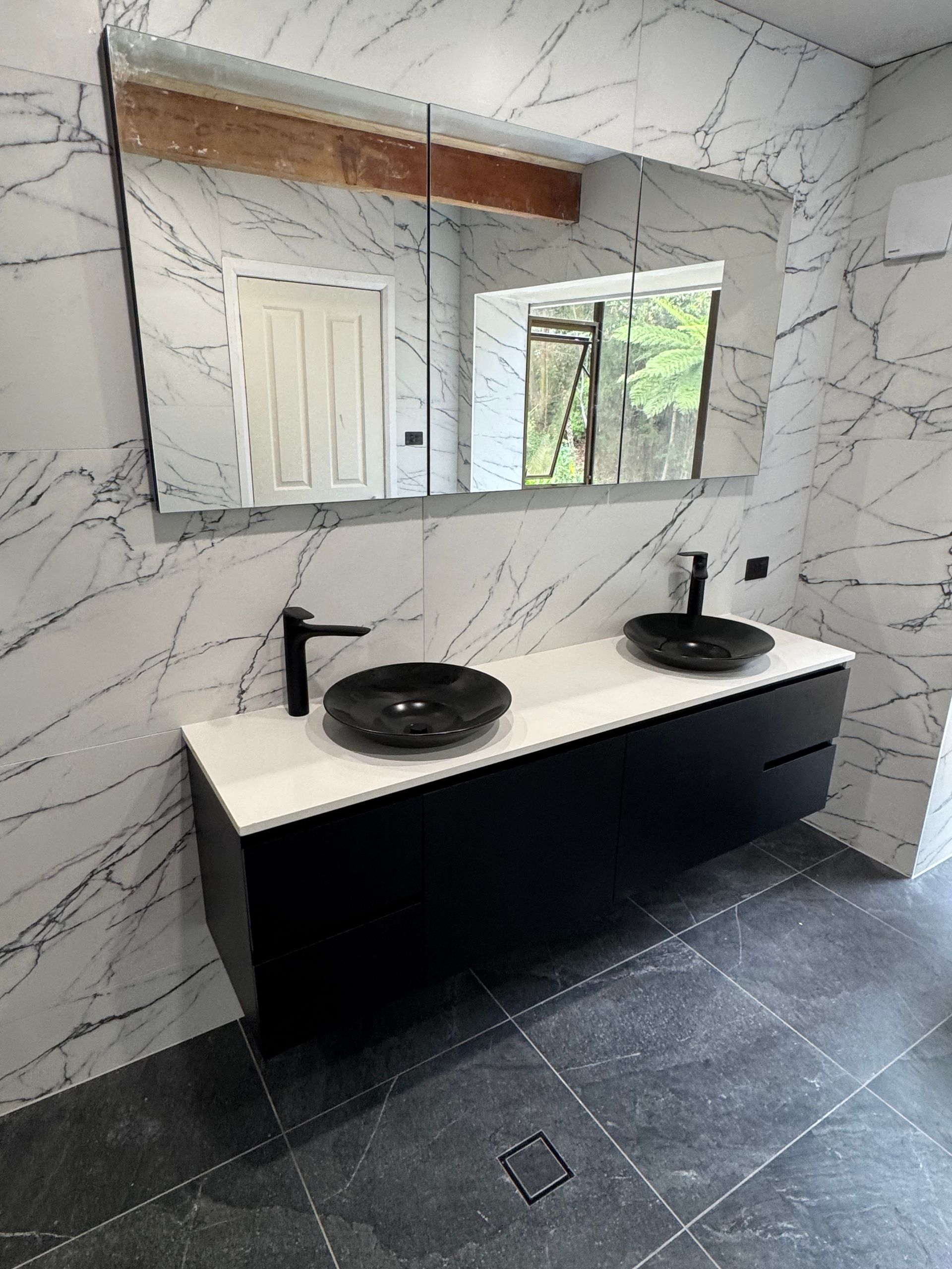 Modern black and white bathroom with a vanity, two black sinks, and a large mirror. Marble-patterned walls — Fair Plumbing In Shellharbour, NSW