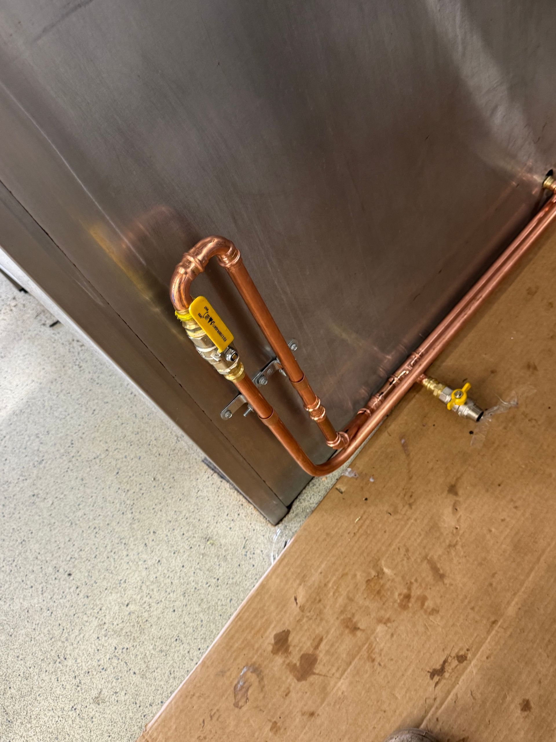 Copper pipes with yellow valves are attached to a stainless steel wall and floor — Fair Plumbing In Shellharbour, NSW