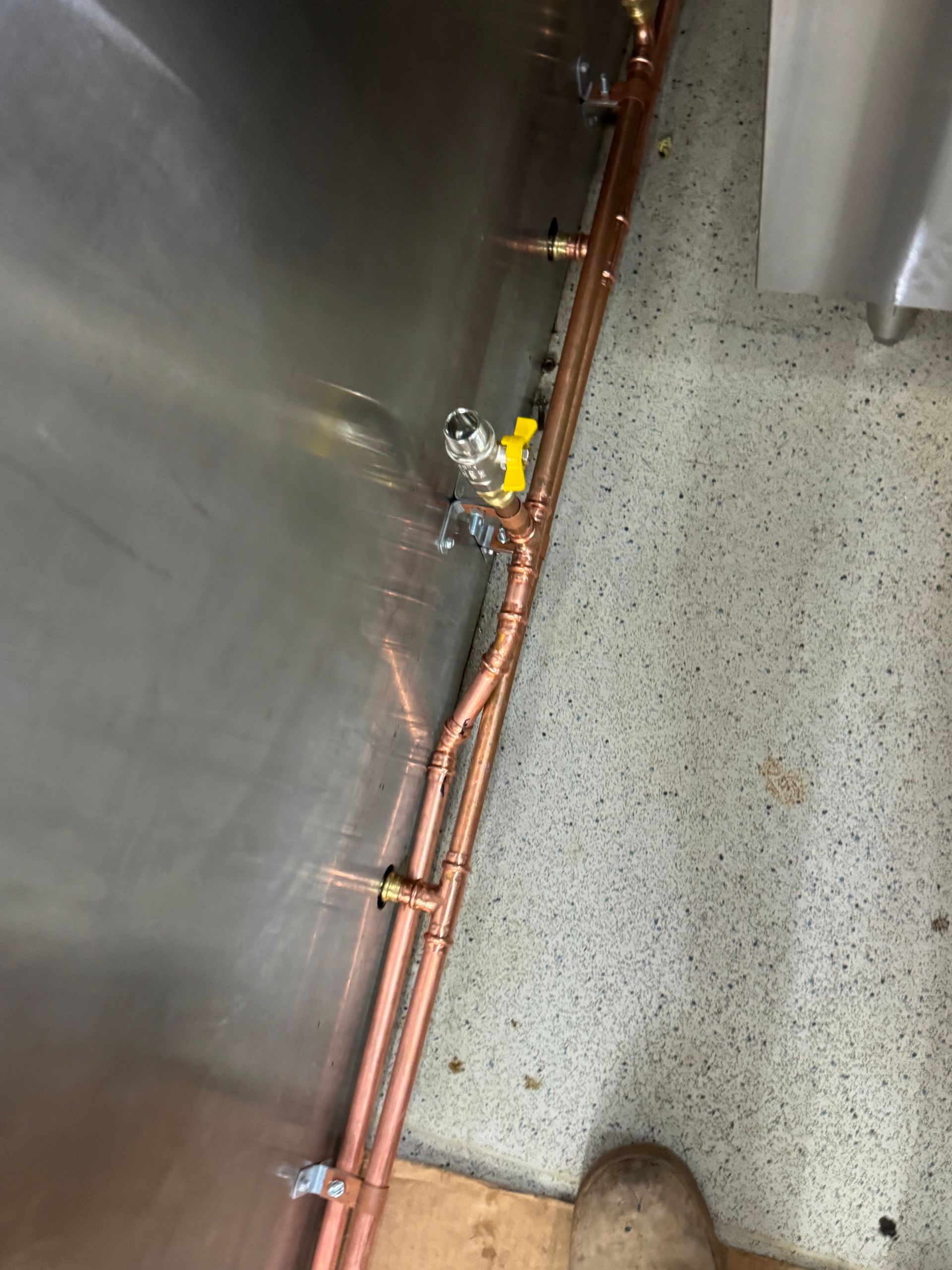 Copper pipes and valves against a metal wall and speckled floor — Fair Plumbing In Kembla Grange, NSW