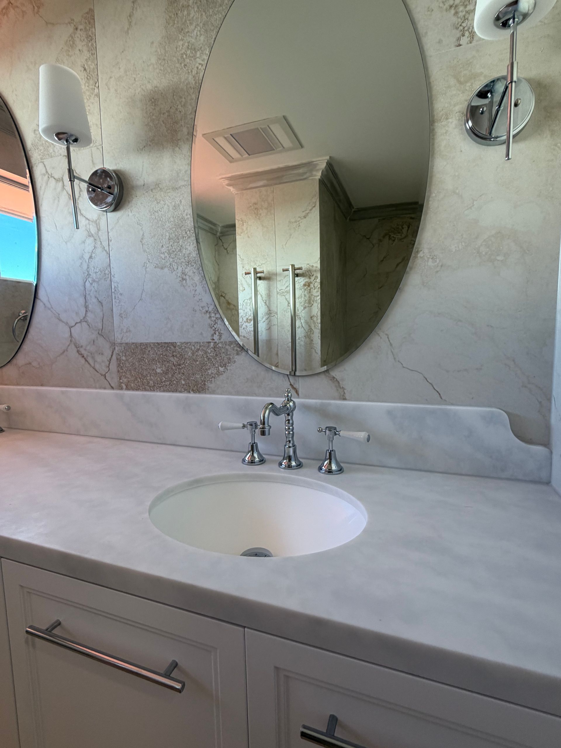 Bathroom vanity with oval mirror, white countertop, sink, chrome faucet, and sconces — Fair Plumbing In Shellharbour, NSW
