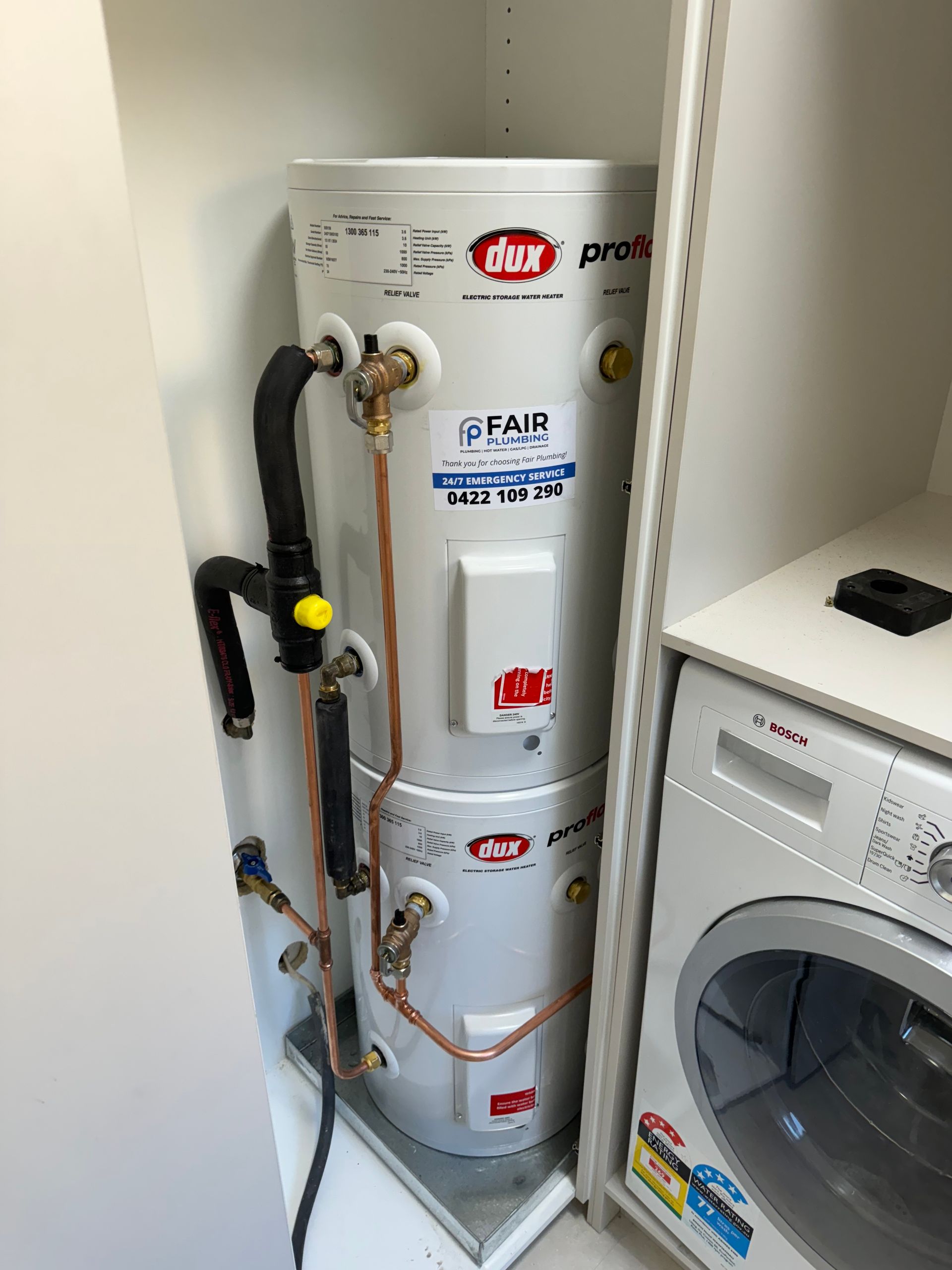 A stacked hot water heater in a laundry room, white cylinders with copper pipes and a washing machine — Fair Plumbing In Dapto, NSW