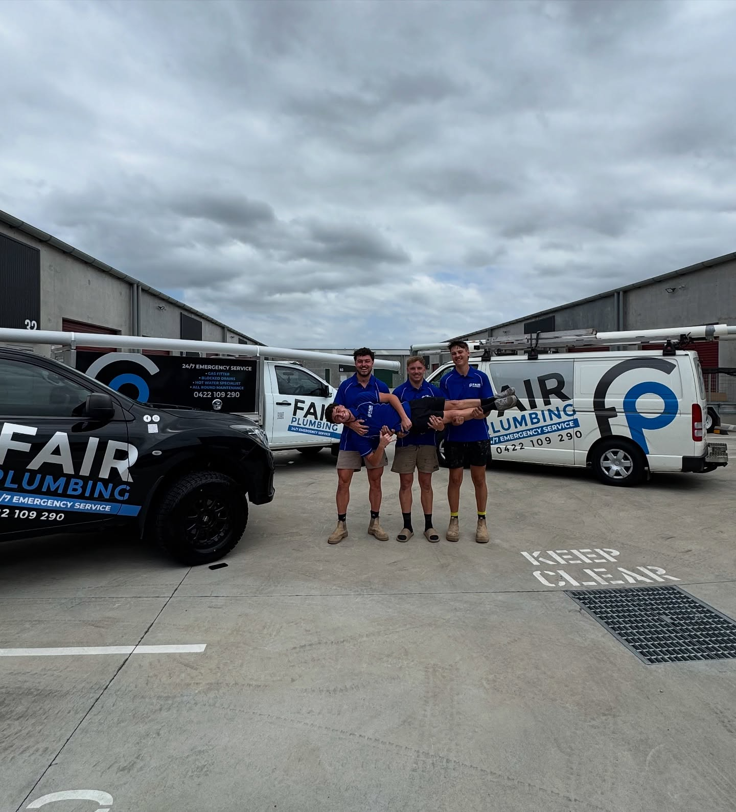 Three Plumbers in Blue Shirts Stand With Their Work Vans — Fair Plumbing In Kembla Grange, NSW