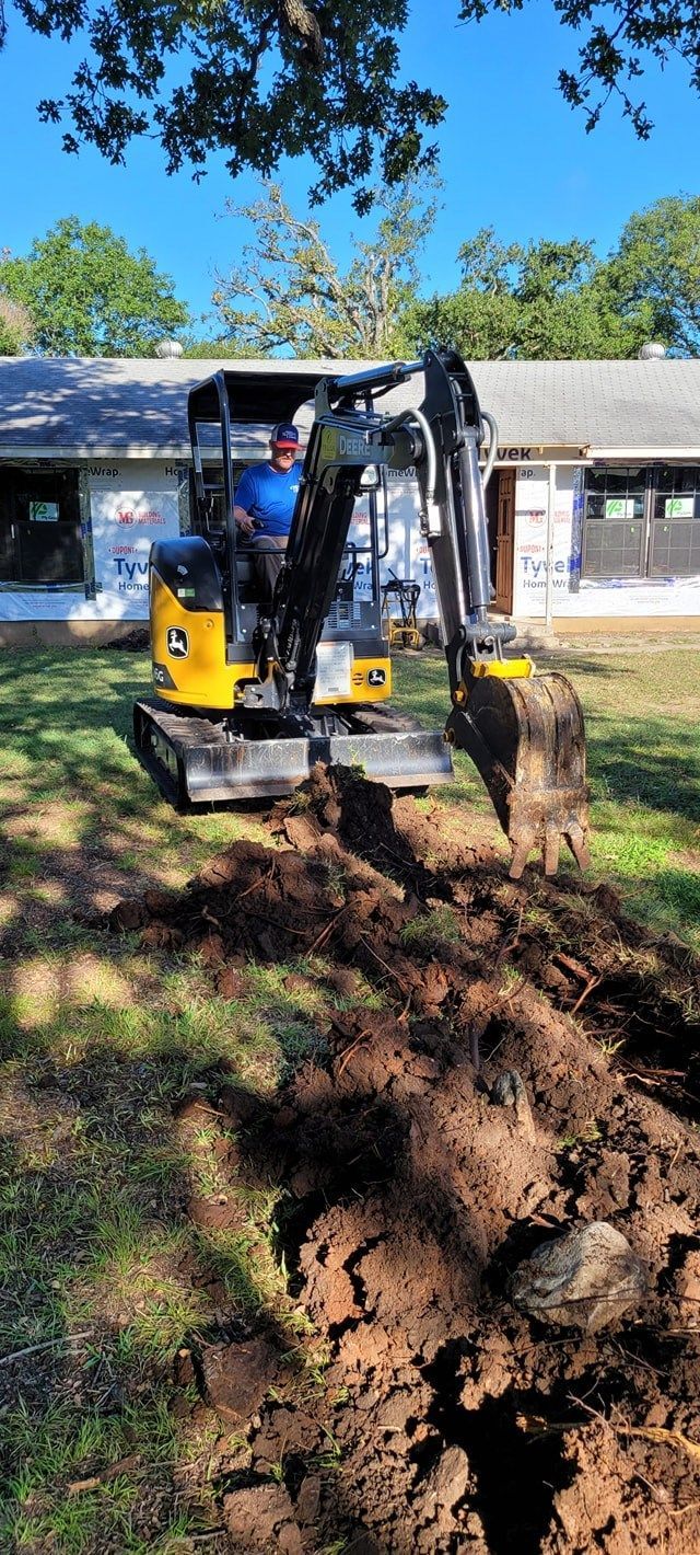 A man is driving a small excavator in a yard.