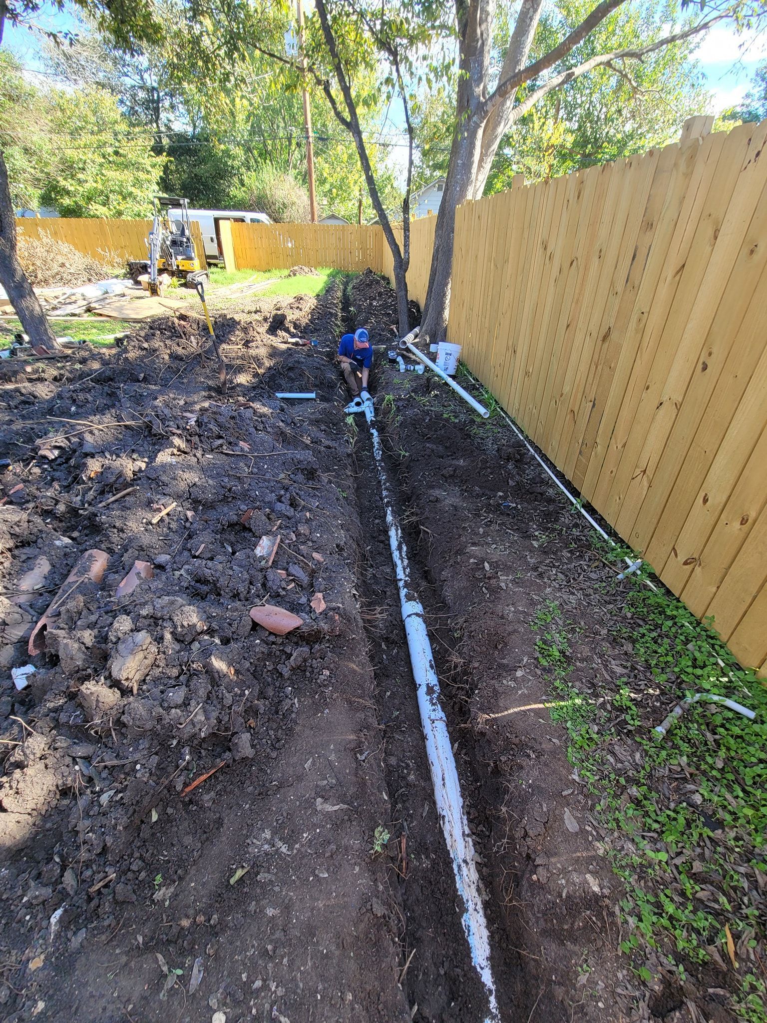 A man is digging a hole in the dirt next to a wooden fence.