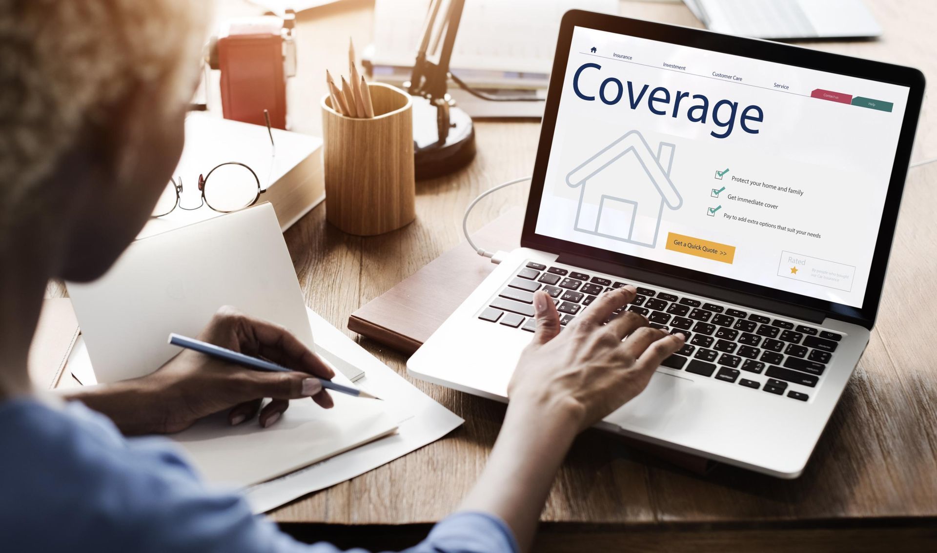 Person working on a laptop, viewing a home insurance coverage website, taking notes.