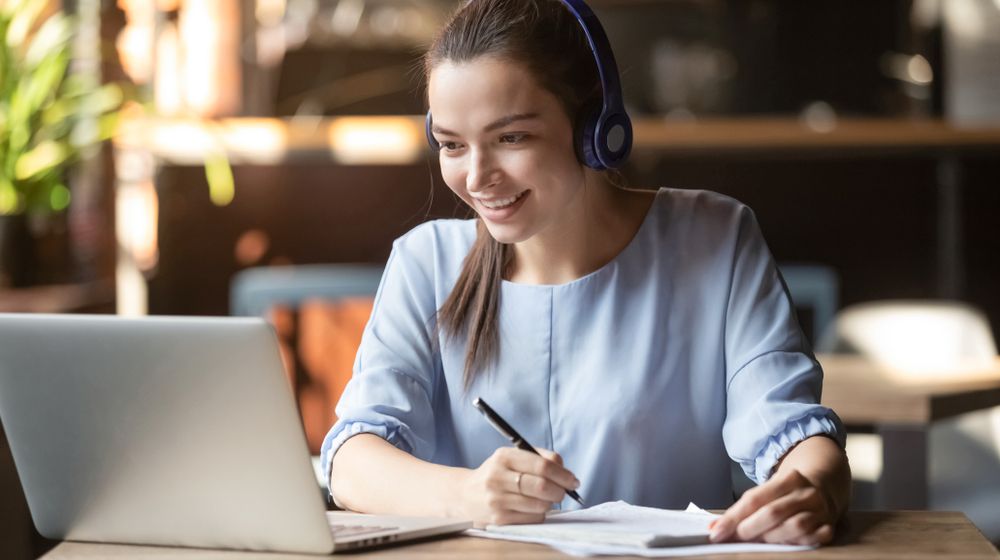 A Woman Wearing Headphones is Sitting at a Table Using a Laptop — Successful Resumes in Gladstone, QLD
