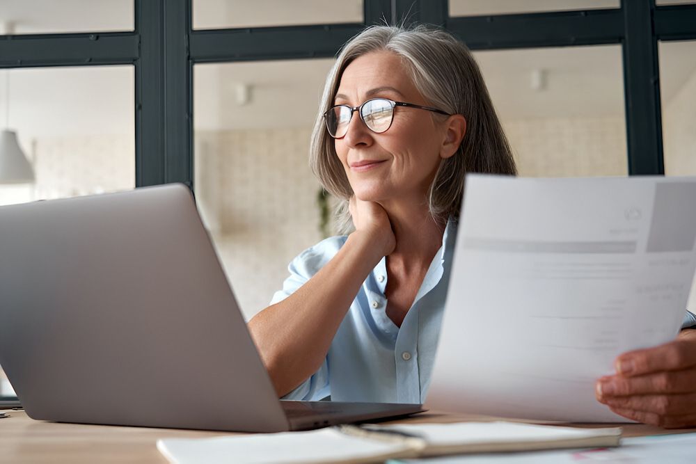 A Woman Is Sitting At A Desk With A Laptop And Papers — Successful Resumes in Wonga Beach, QLD