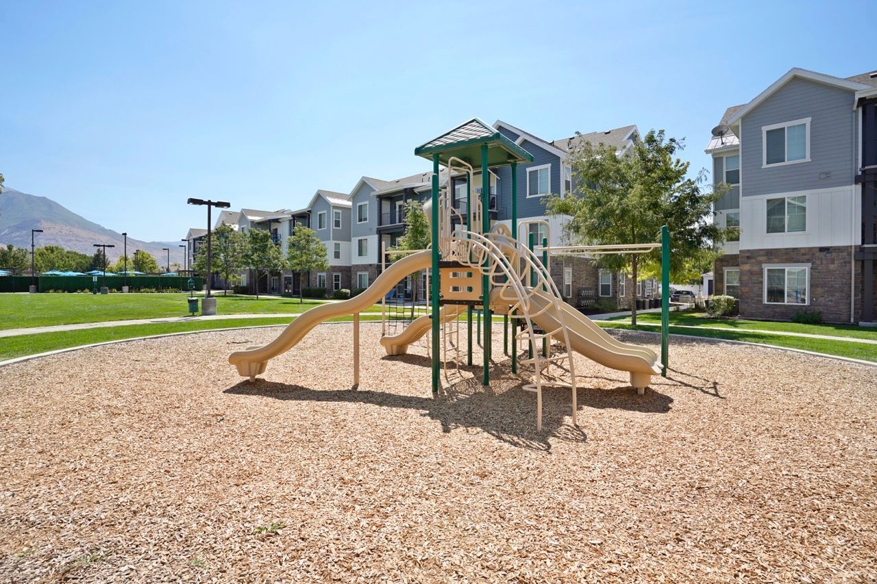 Outdoor playground with beige slides and climbing structure in a grassy apartment complex courtyard.