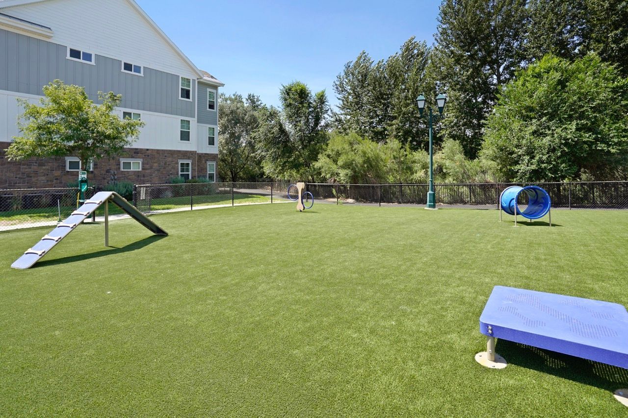 Playground at an apartment community: slide, tunnel, and a blue tube on a grassy, fenced area.