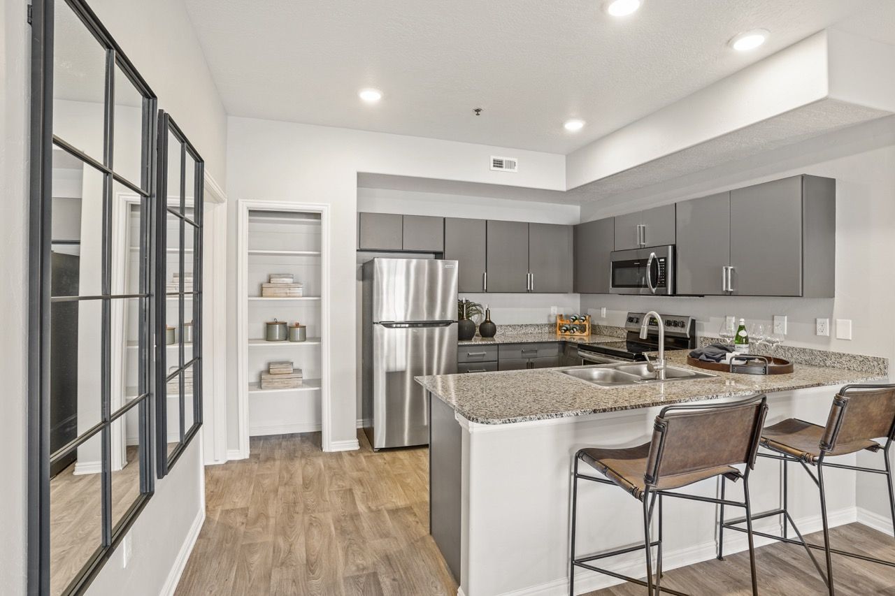 Modern kitchen with granite island, stainless steel appliances, and two bar stools.