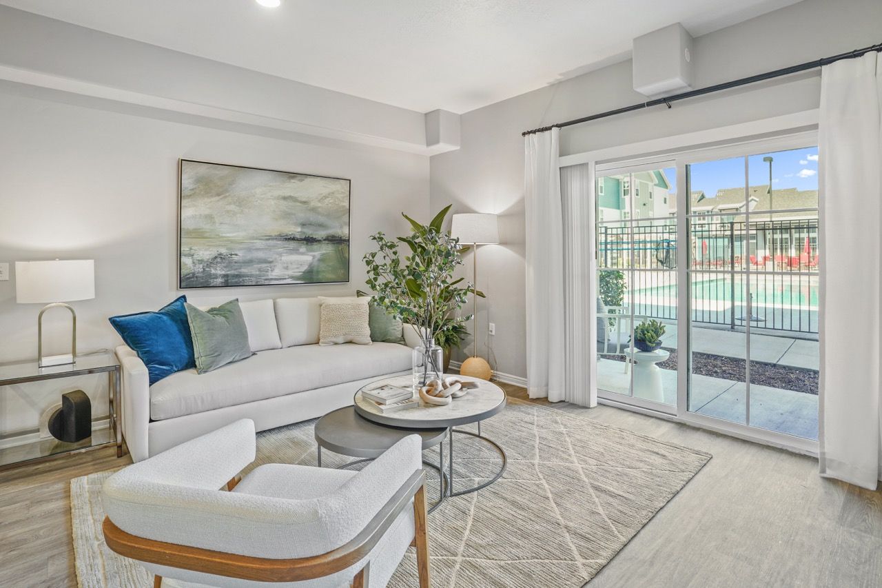 Bright living room with a white sofa, accent chairs, and a sliding glass door to the pool.