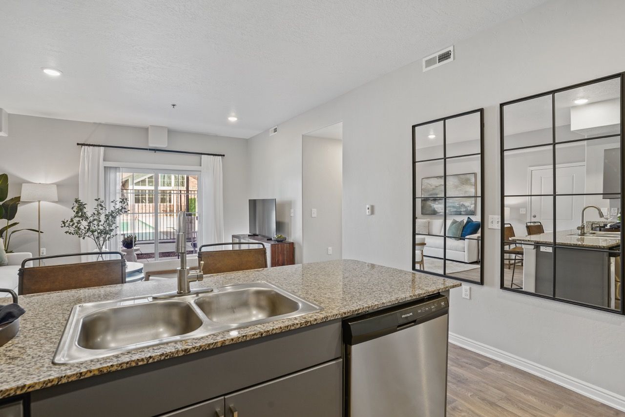 Open-concept kitchen with granite island, double sink, and stainless dishwasher; living area visible beyond.