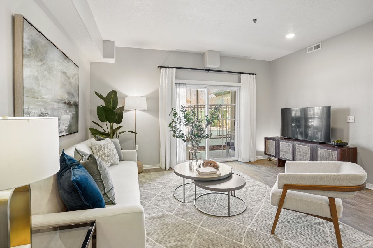 Living room in a modern apartment with sofa, chair, coffee tables, TV, and sliding glass door to a balcony.