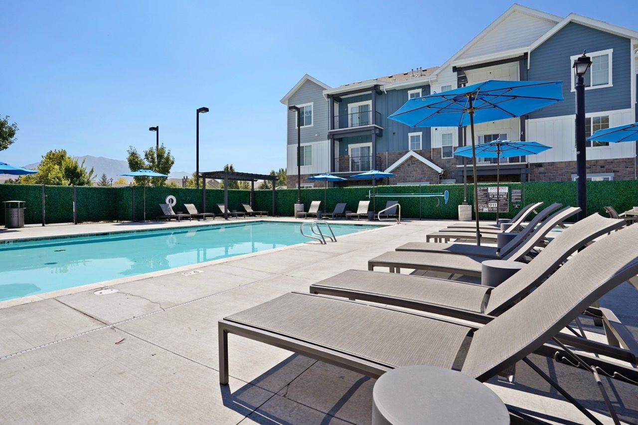 Outdoor pool area at an apartment community with sun loungers and blue umbrellas.