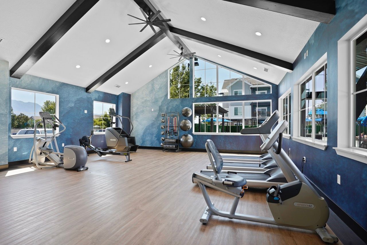 Bright indoor community gym with cardio machines, weights, and large windows.