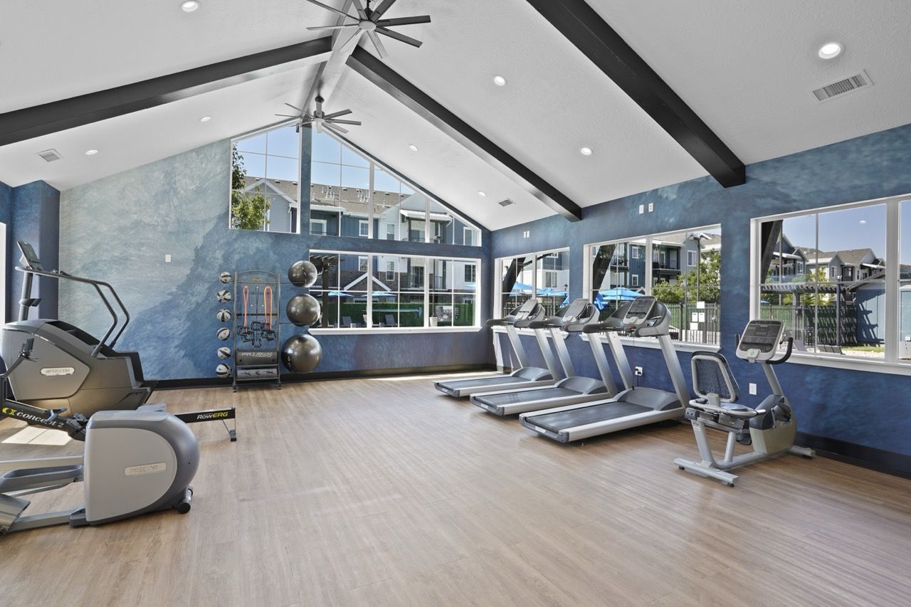 Bright apartment community gym with treadmills, bikes, and weights.
