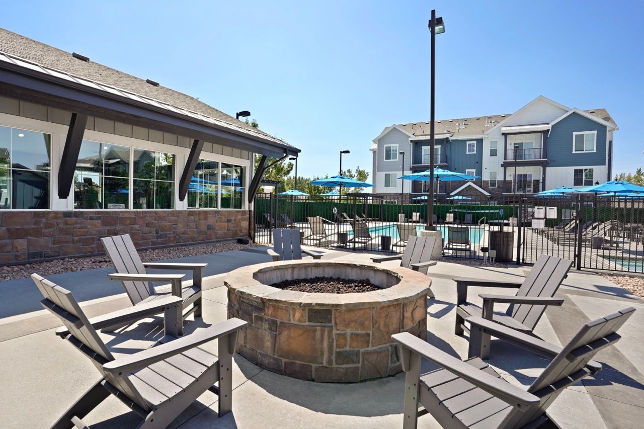 Outdoor community pool area with a circular stone fire pit and surrounding chairs.
