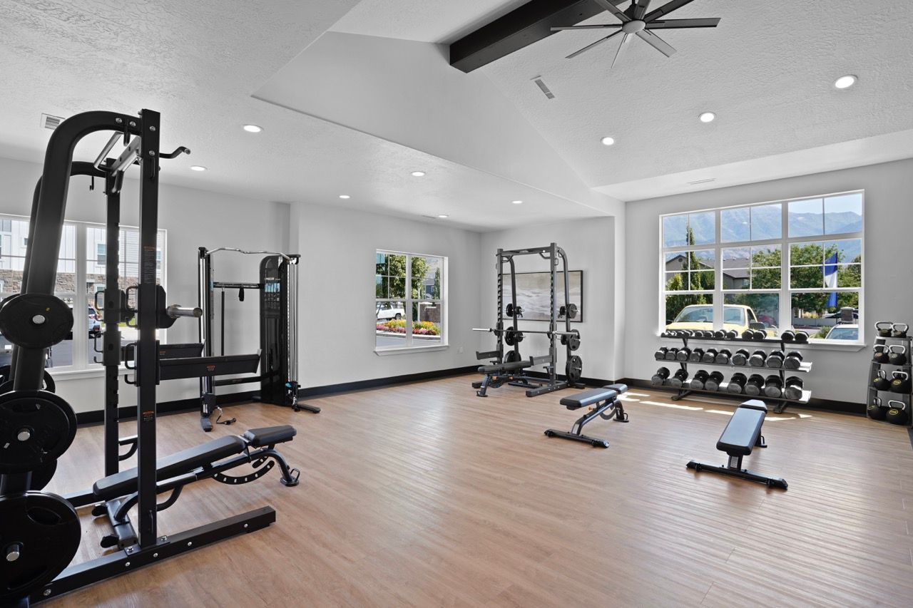 Interior view of a well-lit apartment fitness center with weight machines, free weights, and benches.