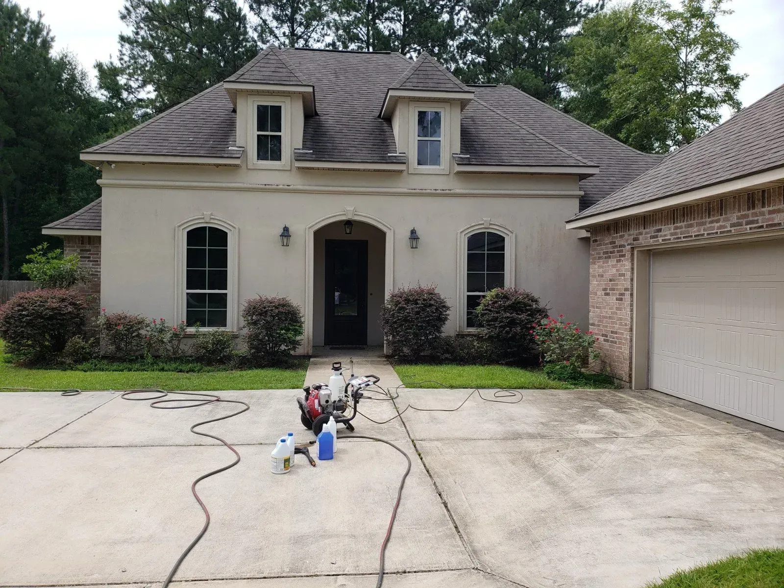 A tan house with a brick garage and driveway, featuring a pressure washing machine and equipment in the center.