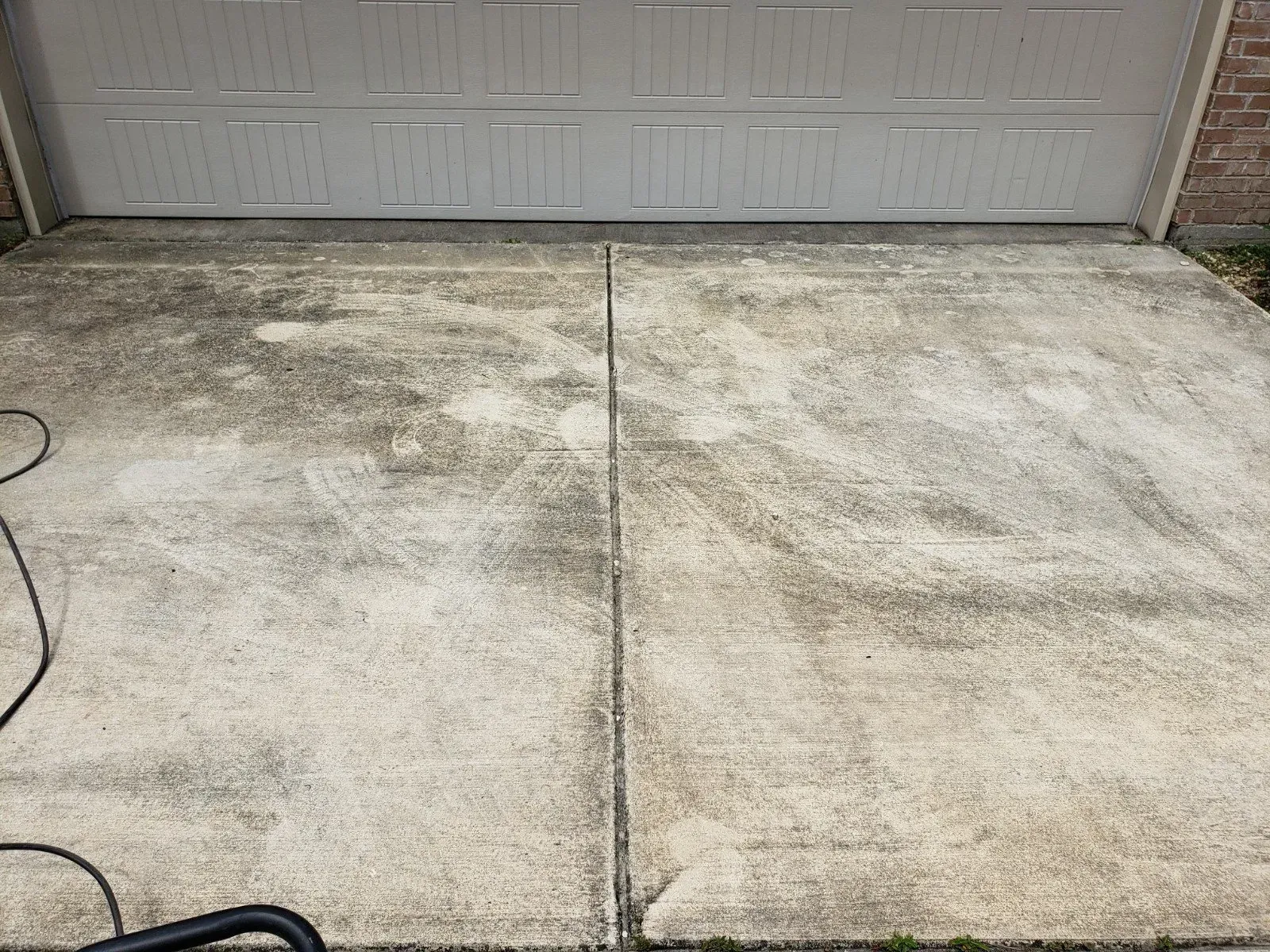 A dirty residential driveway made of concrete with visible cleaning marks and streaks in front of a garage door.