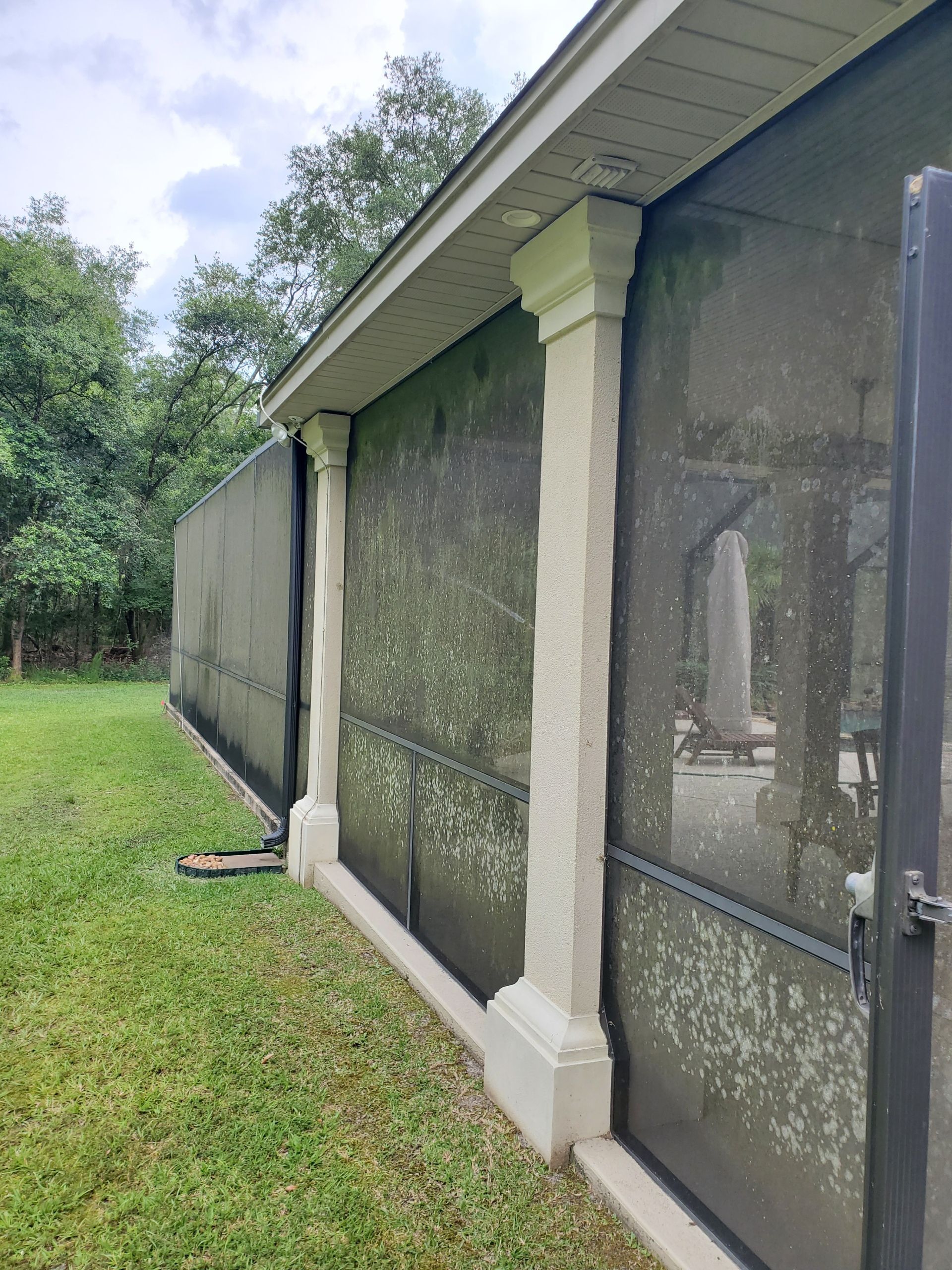 An exterior view of a screened-in patio with off-white textured pillars, siding, and a grassy yard.