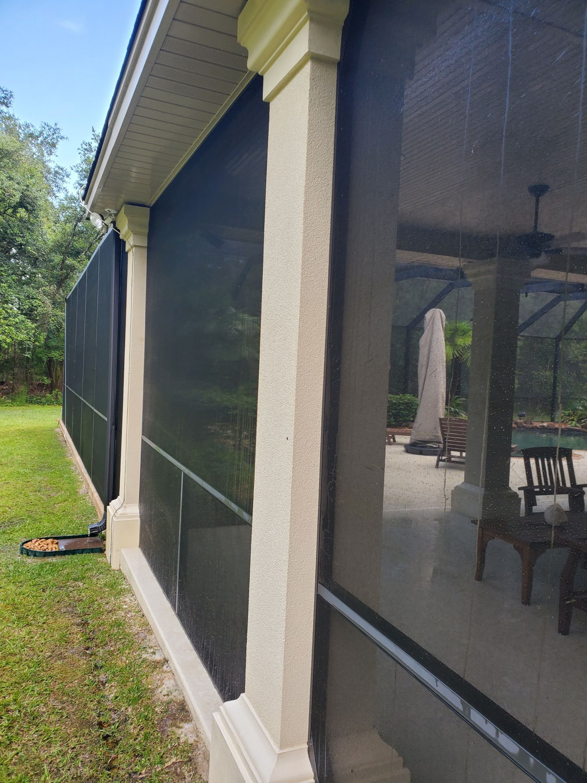 A stucco-covered column stands at the corner of a screened-in lanai overlooking a grassy yard.