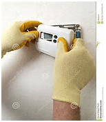 Hands in yellow gloves installing a white thermostat on a white wall.