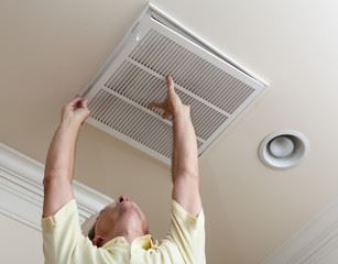 Man removing a white air vent cover from a ceiling.