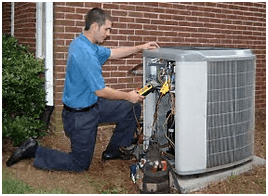 HVAC technician kneels, inspecting an air conditioning unit outside a brick building.