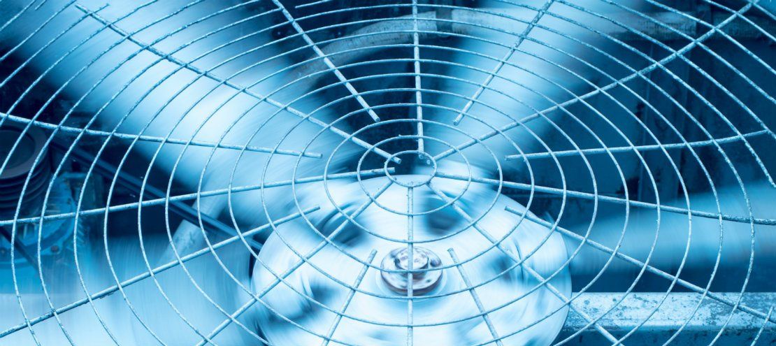 Close-up of a spinning fan, viewed through a protective wire grid. Blue tones.