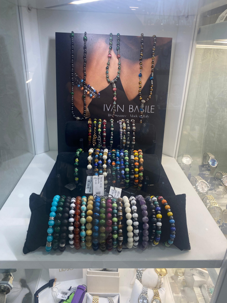 Esposizione di gioielli: collane e braccialetti con perline di vari colori su espositori neri.