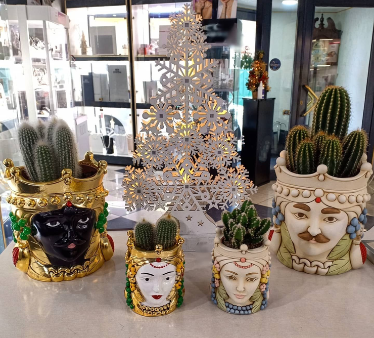 Piante di cactus in vasi di ceramica decorati a forma di viso, con un albero a forma di fiocco di neve bianco in vetrina.