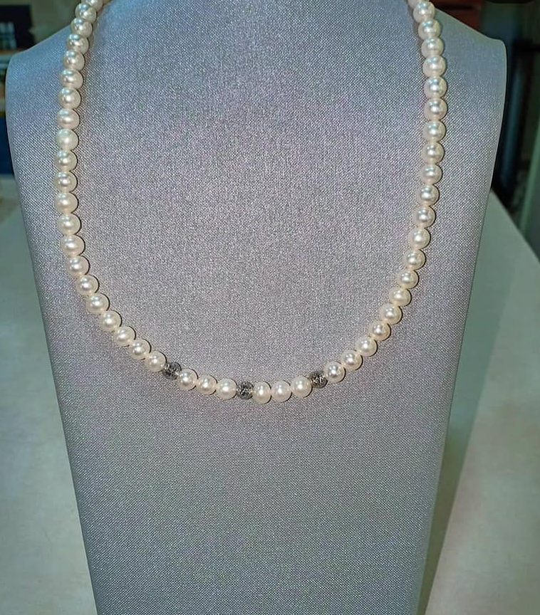 Collana di perle esposta su un portagioielli grigio.