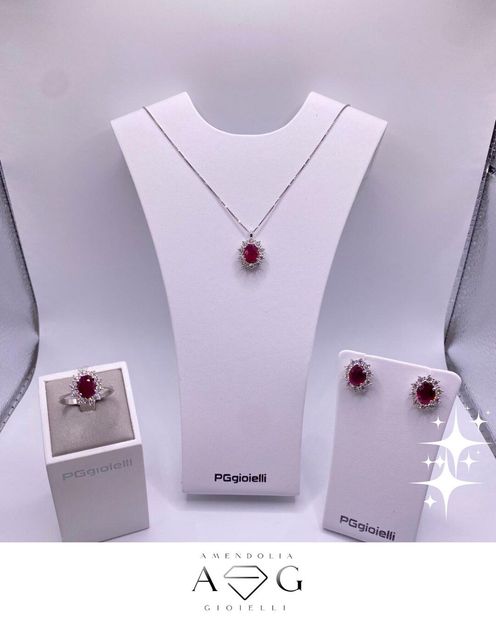 Parure di gioielli con pietre di rubino: anello, collana e orecchini su espositori bianchi.