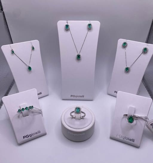Esposizione di gioielli: collane di smeraldi, orecchini, anelli su supporti bianchi.