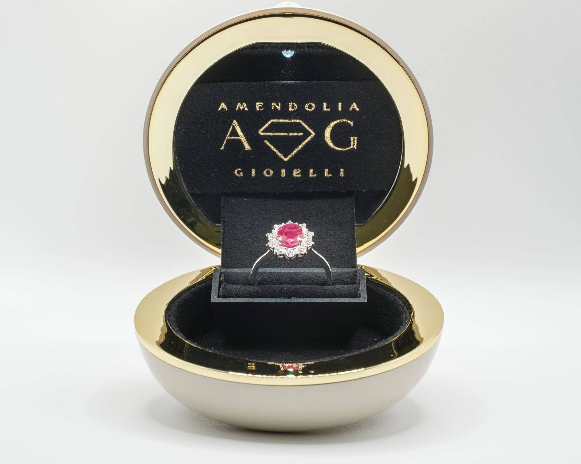 Anello in un portagioie rotondo e aperto. L'anello ha una pietra centrale rossa e pietre bianche circostanti.