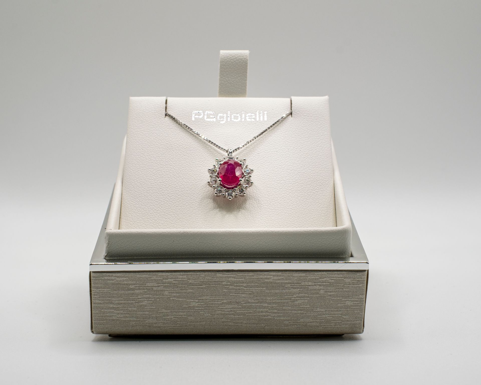 Collana con ciondolo di rubino esposta su un portagioie in velluto bianco all'interno di una scatola d'argento.