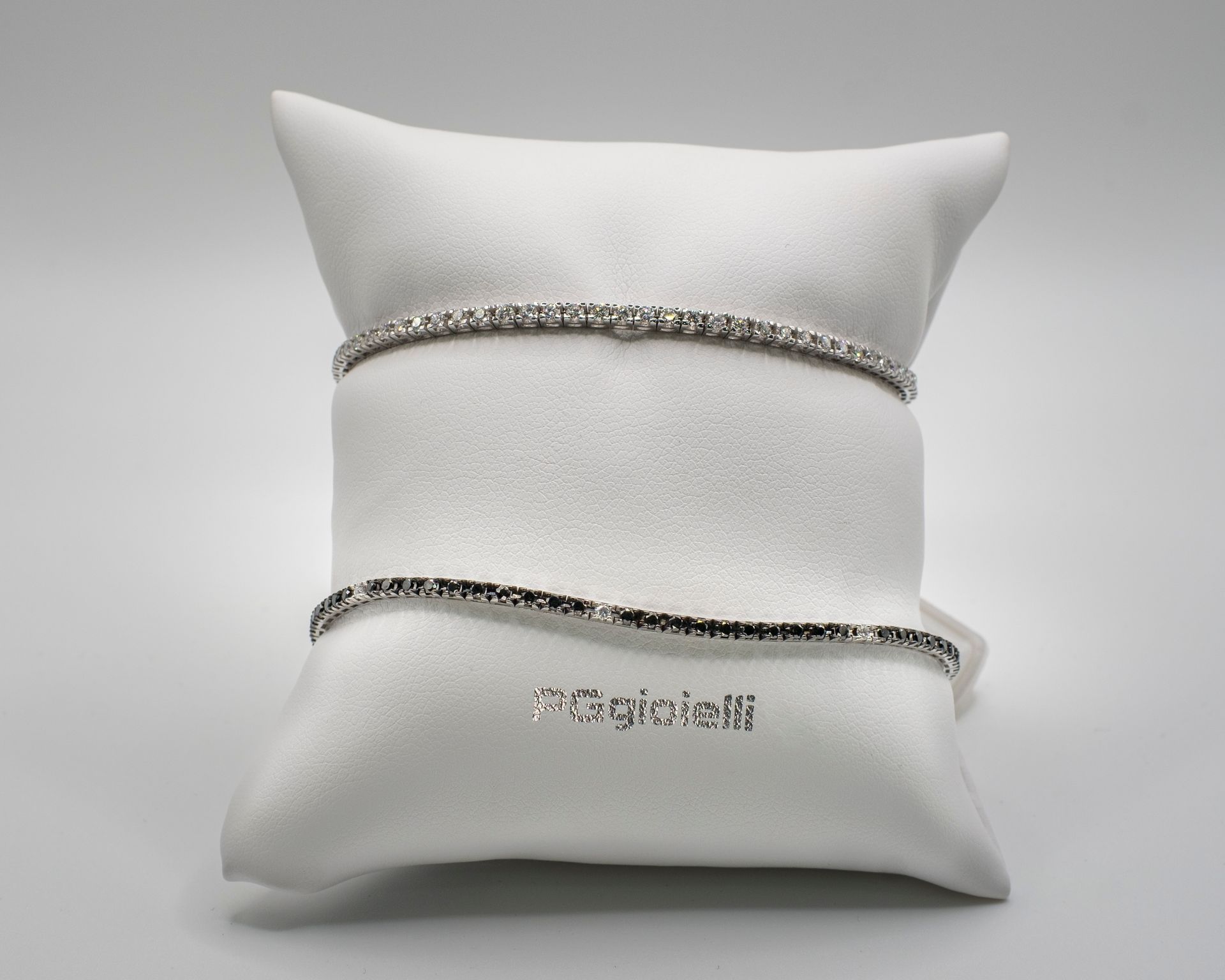Due braccialetti di diamanti su un cuscino di raso bianco con la scritta “gioielli” in argento.