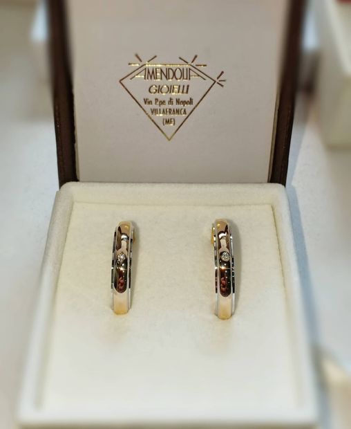 Due orecchini in oro e diamanti in un portagioie con il logo del marchio.